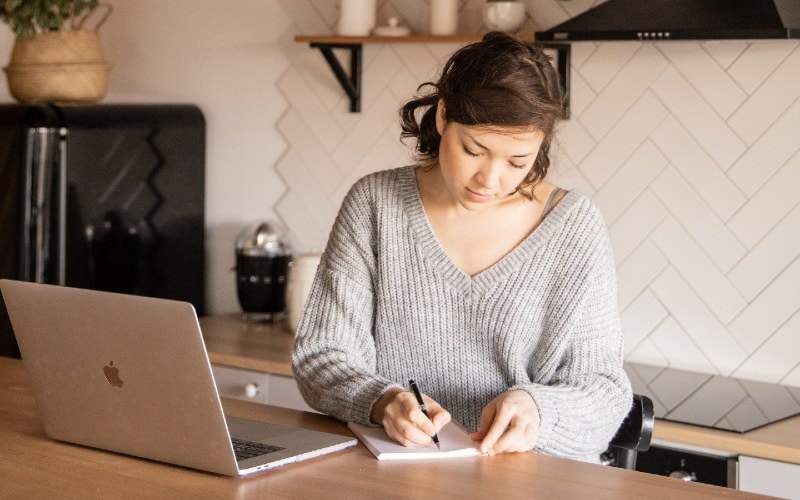 a woman with laptop and notepad in the kitchen